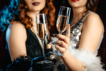 Close up glasses of champagne. Flappers women wearing in style of Roaring Gatsby twenties drinking...