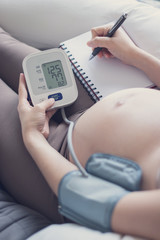 Pregnant woman measuring blood pressure at home, health check of expecting mom