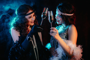 Attractive flappers women dressed in style of Roaring twenties posing on neon smoky background....
