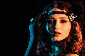Old-fashioned woman dressed in style of Great Gatsby posing on dark background with neon light.....
