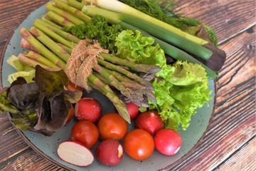 fresh vegetables, green asparagus, radish, green onions, lettuce in a plate on a wooden table
