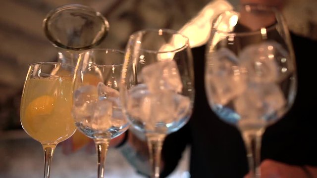 Bartender silhouette fills a set of transparent glass goblets with ice cubes and lemonade on a bar background, close-up.