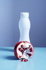 Vertical shot of red bright pomegranate and a white bottle of yogurt in the background on a blue table and gray background. Healthy food and drinks