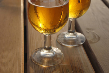 Two glasses of cold beer with condensation on their outsides on a wooden slatted table
