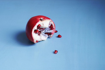Half a pomegranate is on a blue wooden table. Bright, colorful, vivid and vibrant horizontal shot of a combination of red and blue colors - still life