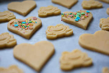 Close up of colourful and happy homemade sugar sprinkled heart and frog shaped butter cookies on a baking paper tray.