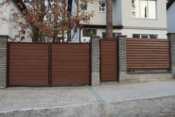 one closed brown private gate and part of the fence from wooden boards and bricks 