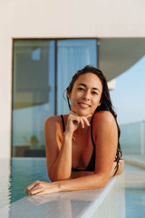 Close up portrait of a beautiful happy woman resting on her hands at the side of a sun bathed swimming pool