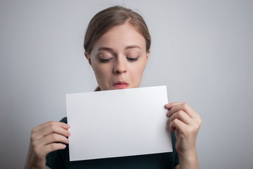 Naklejka premium Smiling young Caucasian woman girl holding blank white paper sheet with copy space