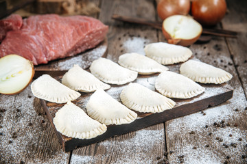 Raw uncooked semi-finished large vareniki dumplings, molded from pastry with a napkin, on a wooden board on a table, horizontal