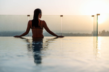 Woman relaxing in infinity pool with sunset city view. Relaxing vacation.  Dubai UAE