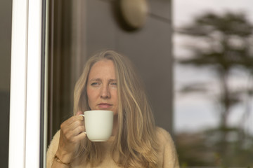Young woman drinking tea, looking through window on a sunny day