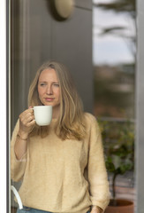 Young woman drinking tea, looking through window on a sunny day