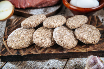 Side closeup view on raw semi-finished frozen cutlets on the wooden board with eggs, onion and potatoes, horizontal