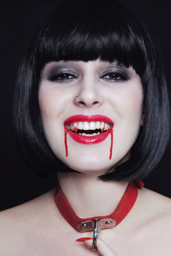 Young beautiful gothic brunette with vampire fangs and blood