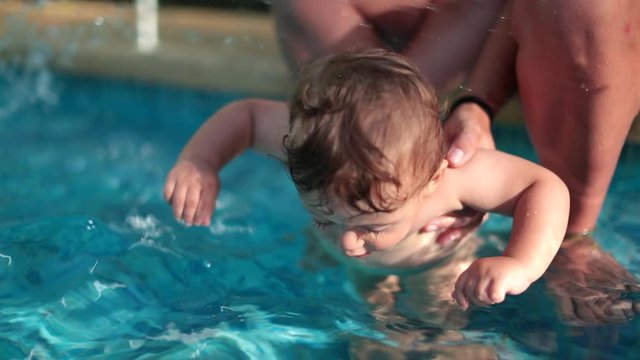 Mother holding baby boy at swimming pool outdoors. Mom teaching toddler. Infant swallowing water