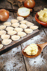 Raw uncooked semi-finished small vareniki dumplings with a filling on a wooden board on a table, vertical format