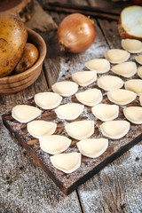 Fototapeta na wymiar Raw uncooked semi-finished small vareniki dumplings with a filling on a wooden board on a table, vertical format