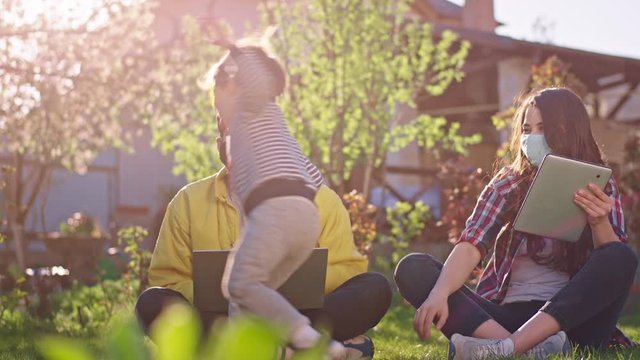 In the garden parents working from home using tablet and laptop wearing protective mask while their son playing funny around them pandemic Coronavirus China 2019