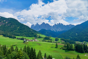 Obraz premium Beautiful landscape in the Dolomites, Italy. A small village surrounded by coniferous forests, green meadows and high mountains. Active summer outdoor recreation, travel, camping.