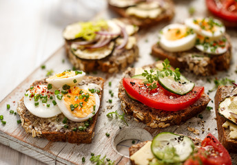 A set of breakfast sandwiches made from homemade buckwheat bread with various toppings on a wooden rustic board, close up