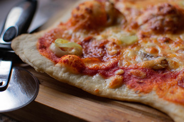 An authentic rustic Italian pizza covered in mozzarella, peppers, cheese, tomato puree sauce and roasted garlic served on wood with a metal pizza cutter