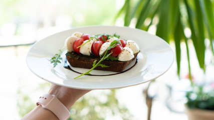 sandwich with mozzarella cheese and cherry tomatoes on a plate in womans hand