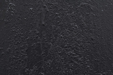 Cracked surface of an old wall or floor painted with black oil paint over an old layer of paint. On the wall there are many small cracks and bumps in the form of a grid of different sizes and shapes.