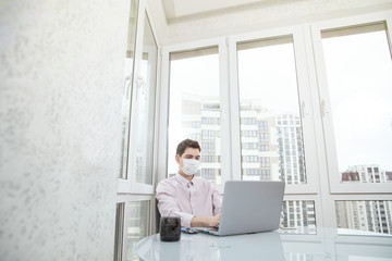 A guy in a protective face mask works at a computer from home during a virus epidemic. Quarantine during viral infection