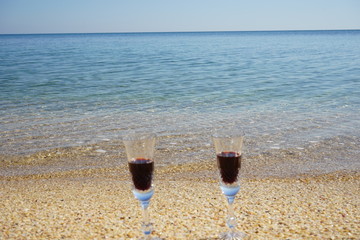 two crystal glasses of red wine against the background of a calm transparent sea and a sandy beach