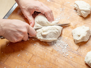 Female hands cut with a knife a kneaded dough on a wooden table. The process of preparing fresh elastic baking dough. Table and hands in flour. Natural home cooking.