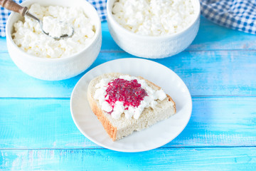 fresh cottage cheese in white bowls and spoons close-up and a sandwich with cottage cheese and raspberry jam on a plate. cottage cheese in bowls on the table and a sandwich with cottage cheese.