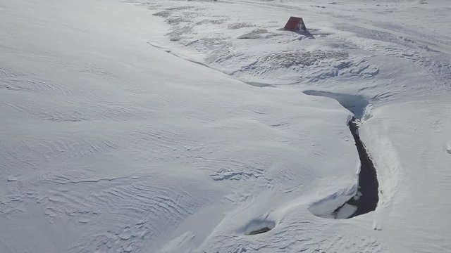 Aerial: Flying Around a Small Cozy House in the Middle of nature. Everything Covered by Fresh Snow. Beautiful sunny day. Amazing landscape background concept.