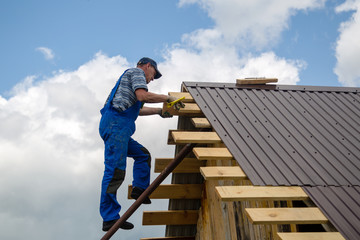 a worker with an electric screwdriver covers the roof with metal sheets