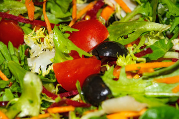 Vegetable salad sliced tomatoes, carrots, beets, lettuce, arugula and olives. Close-up background image.