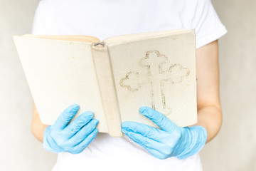 Young woman in white t-shirt reading Bible in blue disposable protective rubber gloves