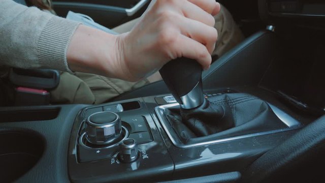 Hand of beautiful young woman driver in beige blouse turn on neutral speed, puts on parking, sharply engages gear shift, puts pressure on gas close up. Girl drive, control auto and change gear. Inside