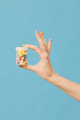 Close-up of female hand holding bottle with capsules and pills over blue background