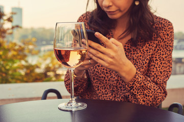 Beautiful elegant woman drinking wine and using cellphone outdoors.