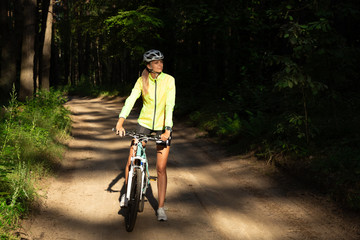 Fototapeta premium A beautiful girl in a bright green windbreaker, shorts and a helmet rides a bicycle in the forest