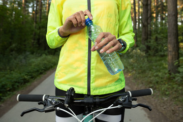 Close-up of a girl's hand in a bright green windbreaker on a bicycle that holds a water bottle