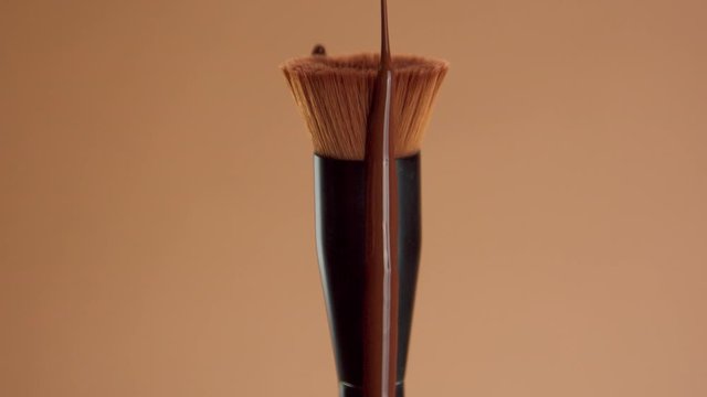 a round foundation brush with a liquid foundation for a deep skin tones covering it. Cosmetics for a deep skin tones dripping from round foundation brush