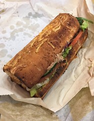 A toasted tuna fish grinder on herb and cheese bread unwrapped and sitting on the packaging 
