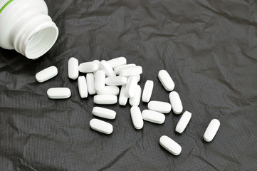 white pills fall out of the can on a black background.