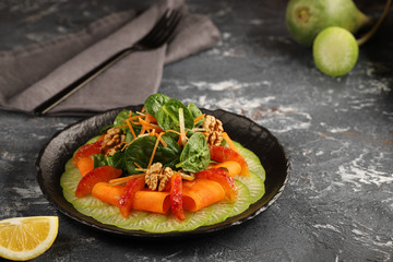 Green radish carpaccio on a black plate, with a salad of spinach, thinly sliced ​​carrots and walnuts, with segments of red oranges.Tasty and healthy food.