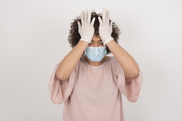 Exasperate female wearing medical mask keeps hands on temples, feels strong headache, closes eyes...