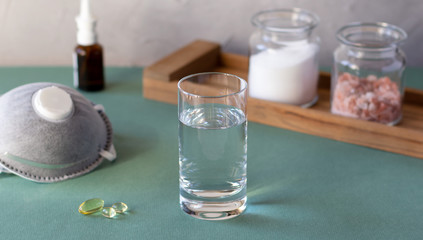 Glass with salty water to rinse nose and throat as prevention and protection from viruses. Medical mask and pills. Covid-19 concept