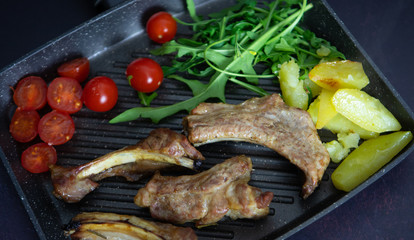Pork ribs with rosemary and tomato and potatoes on cast iron pot, top view