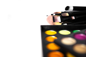 Two eye shadow palettes lie on top of each other next to a set of makeup brushes isolated on a...
