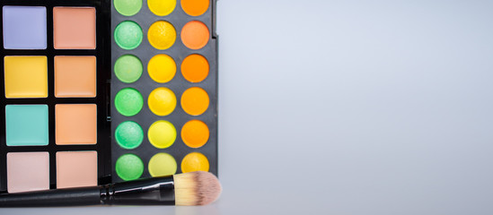 Eyeshadow palette, concealer set and makeup brush on a grey background